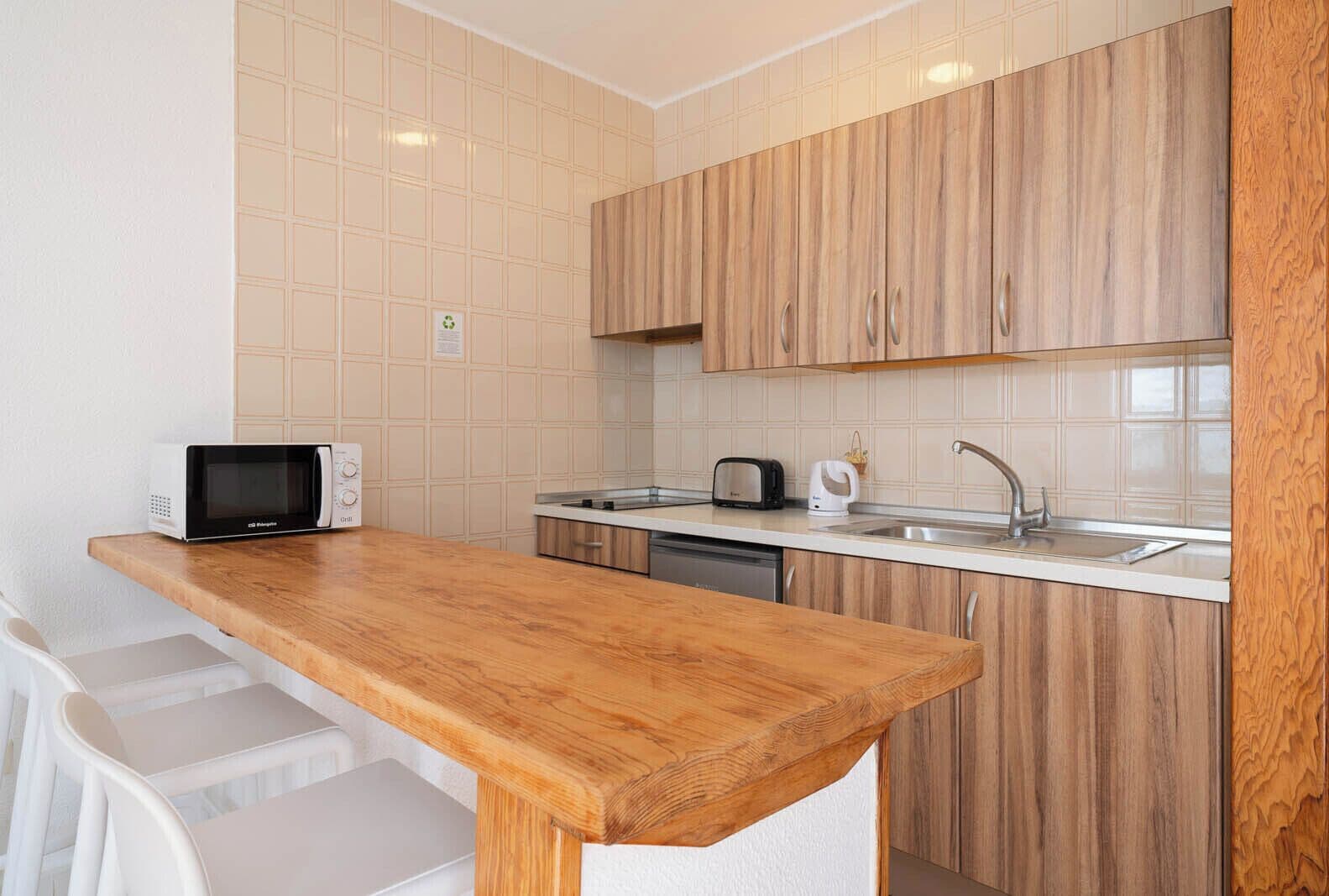 A compact kitchen with wooden cabinets, a microwave, toaster, kettle, and a sink.
