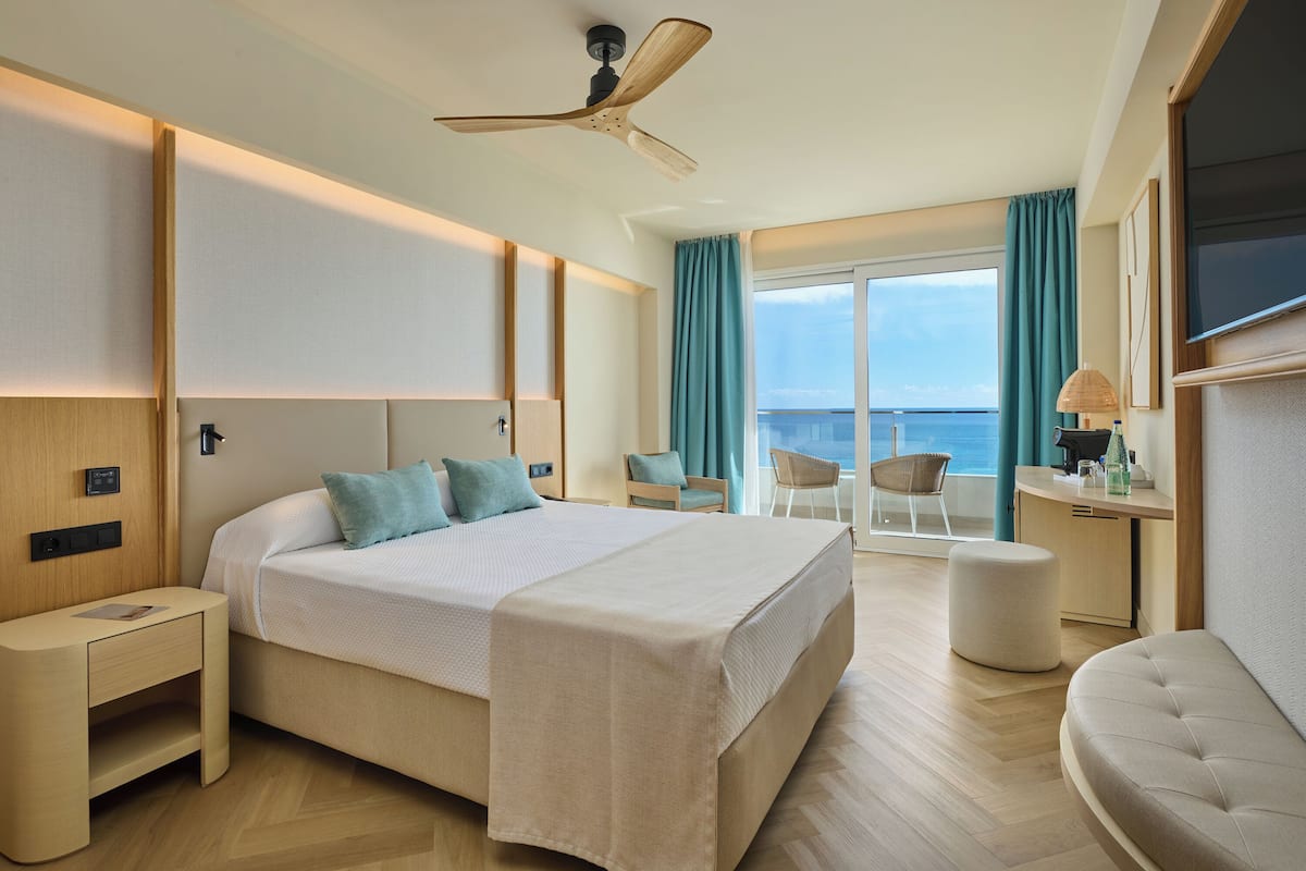 Ein modernes Hotelzimmer mit Bett, Nachttisch, Schreibtisch, Stuhl und Meerblick.