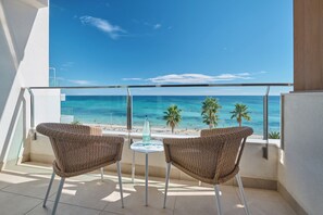 Un balcon avec deux fauteuils en osier et une petite table, donnant sur une plage bordée de palmiers et sur l’océan.