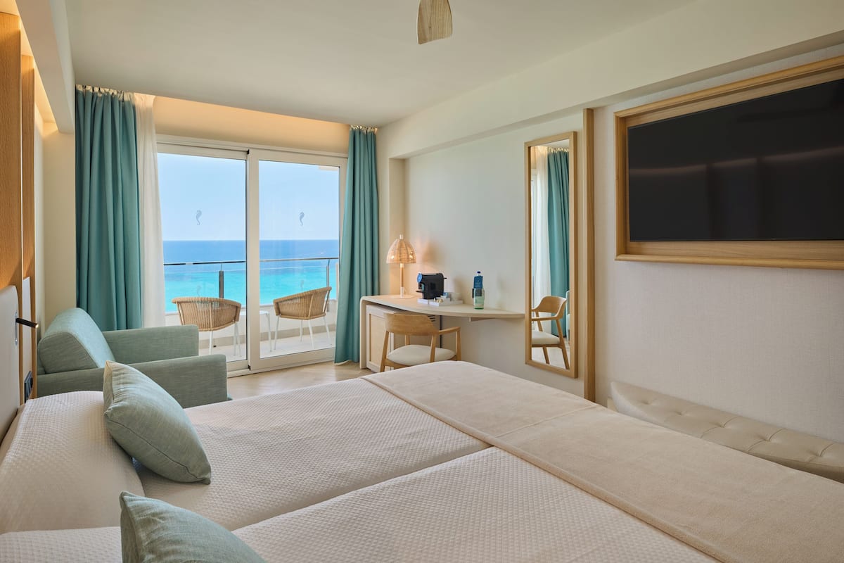 Ein Hotelzimmer mit Bett, Schreibtisch, Stuhl und einem großen Fenster mit Meerblick.
