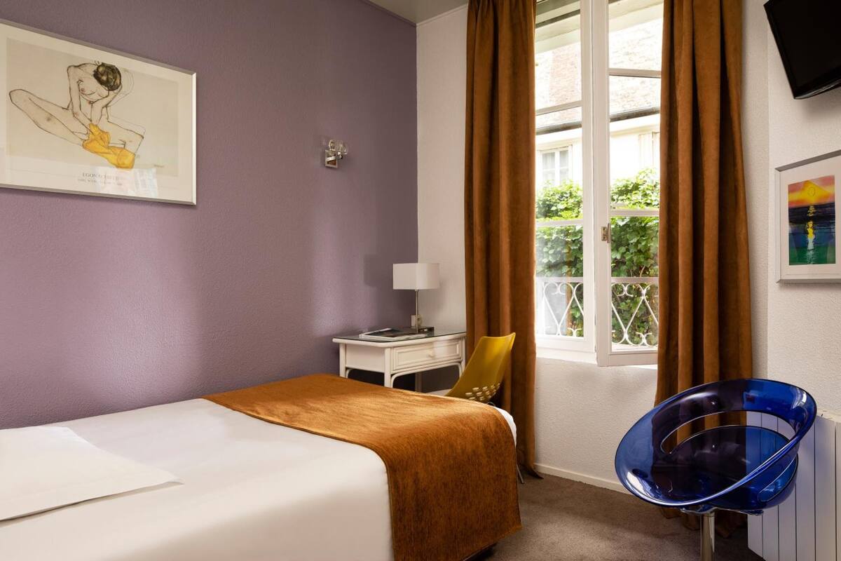 A hotel room with a bed, a desk, a chair, and a window with curtains.