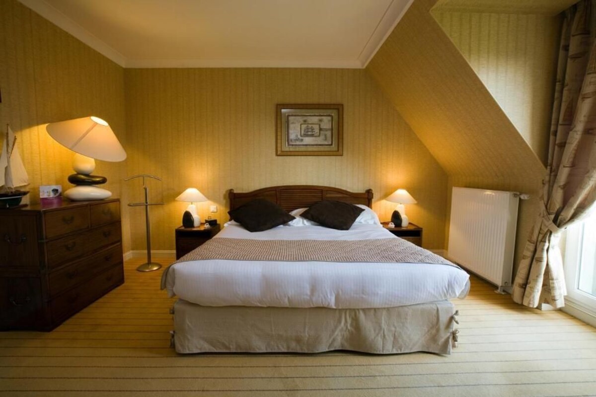 Ein Schlafzimmer mit einem großen Bett, zwei Nachttischen mit Lampen, einem Schminktisch und einem gerahmten Bild an der Wand.
