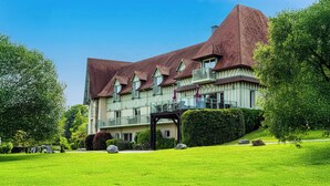 A large, multi-story building with a steeply pitched roof, multiple balconies, and a well-maintained lawn.