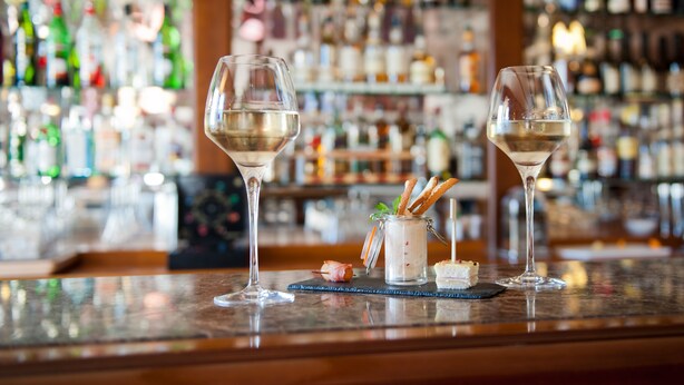 A bar counter with two wine glasses and a small jar of snacks.