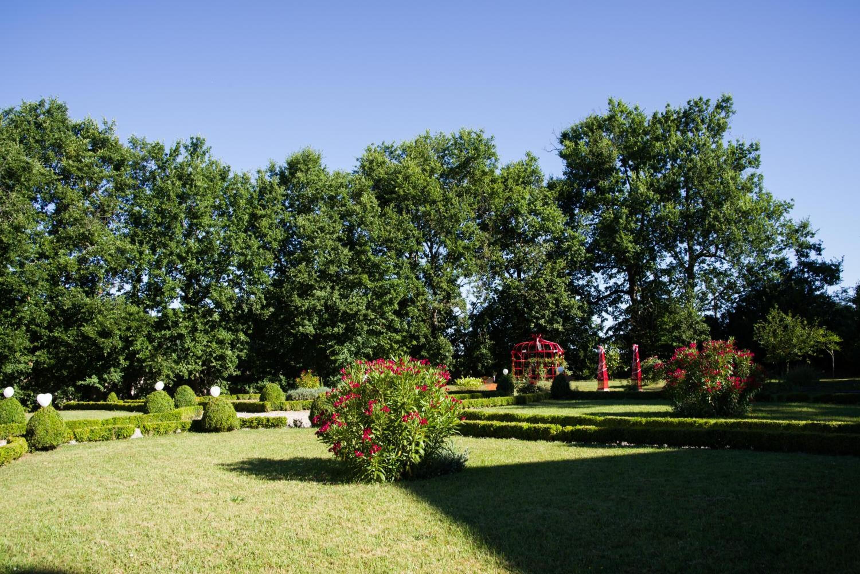 A well-maintained garden with neatly trimmed hedges, a variety of trees, and a small red gazebo.
