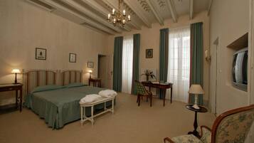 A hotel room with a large bed, a desk, a chair, and a television.