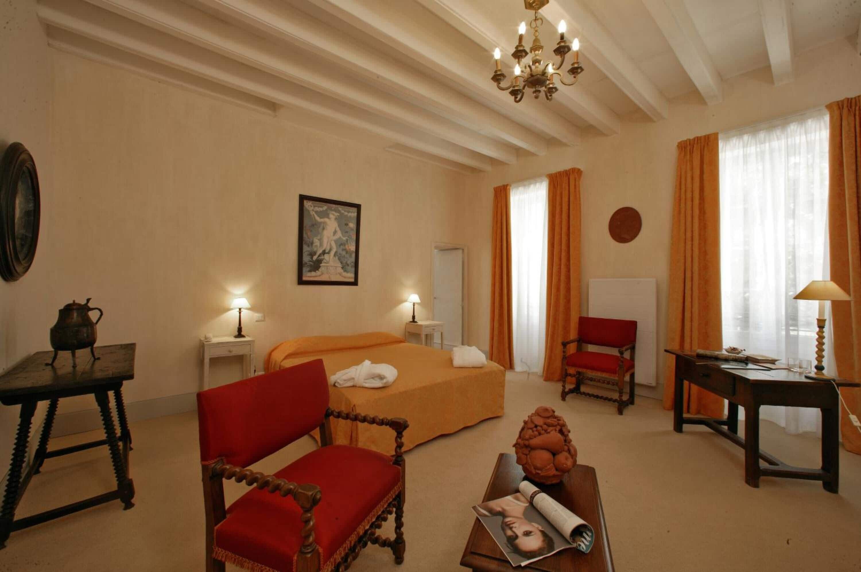 Ein Hotelzimmer mit einem Bett, zwei Stühlen, einem Schreibtisch, einem Tisch, einer Chandelier und einem Bild an der Wand.