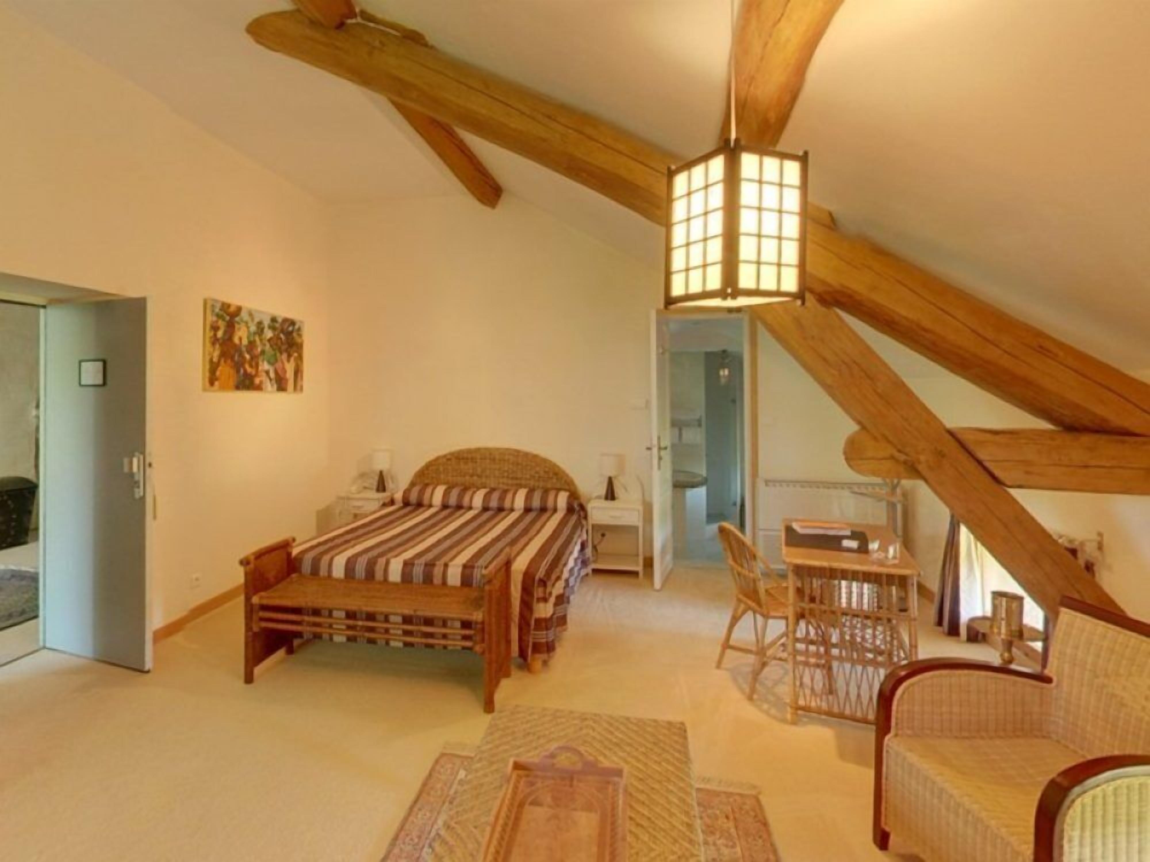 A cozy attic bedroom with a bed, a chair, a small table, and a hanging light fixture.