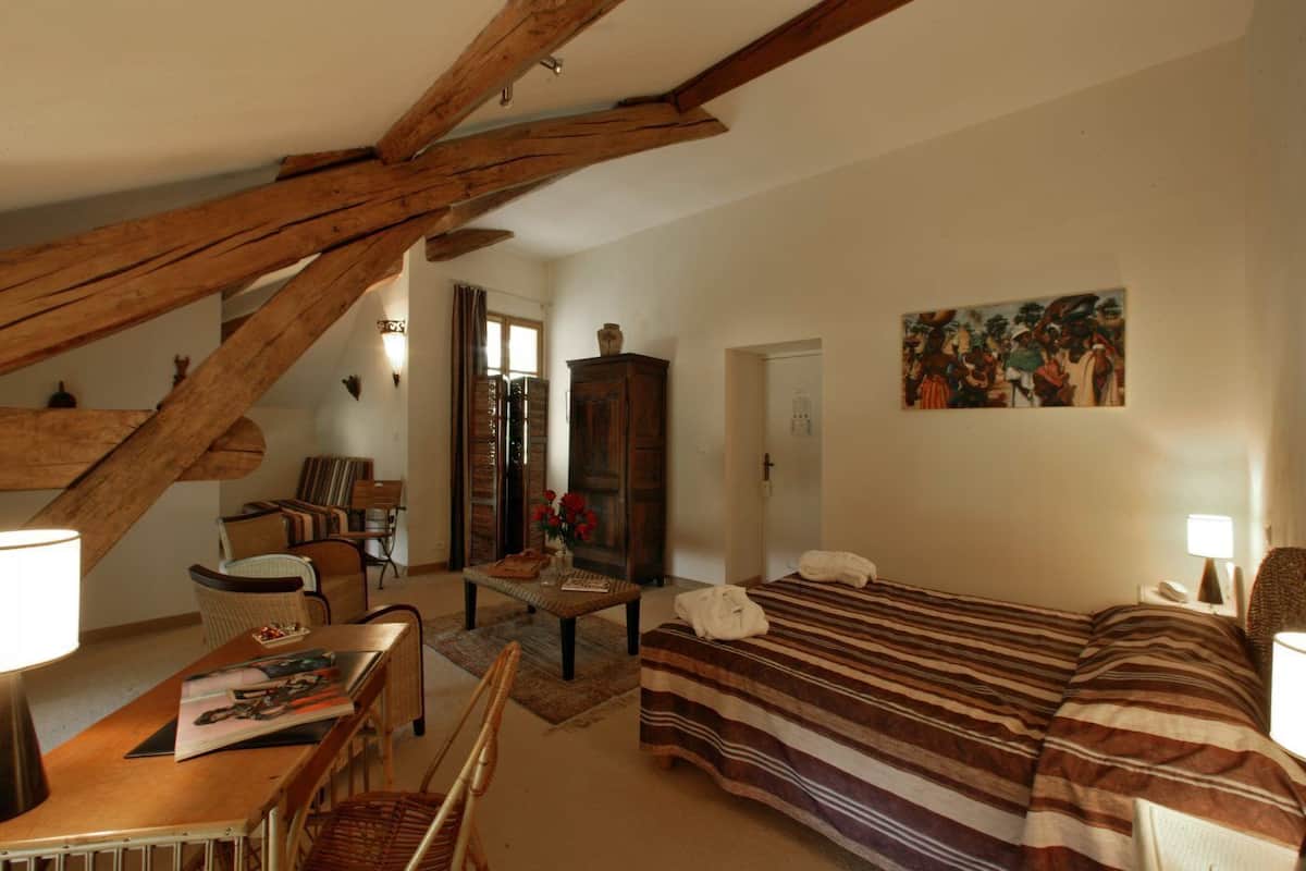 A cozy room with a bed, a desk, and a chair. There is a wooden staircase and a painting on the wall.