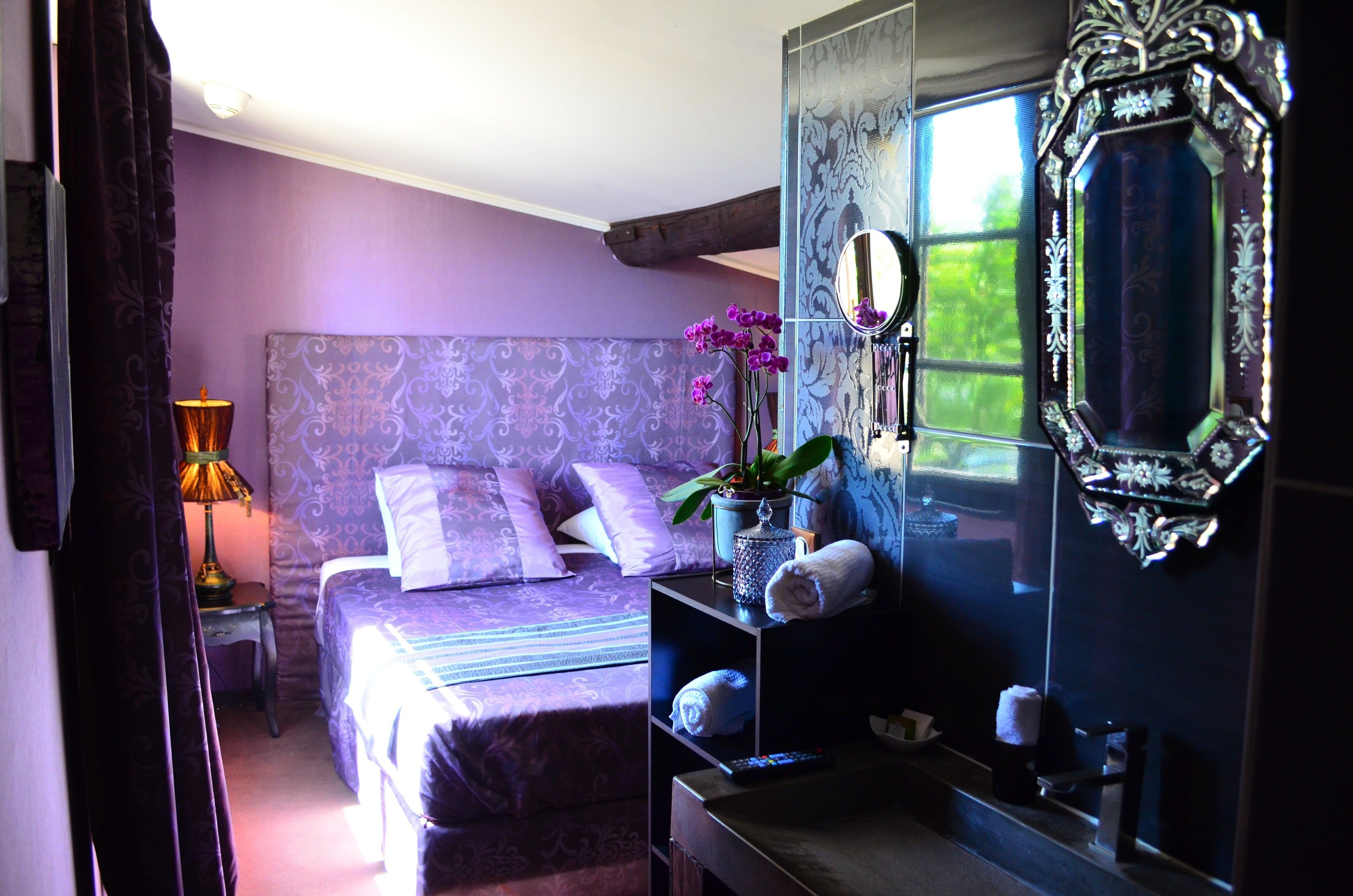 Un dormitorio con cama, una mesita de noche con lámpara, un espejo y una ventana con vistas.