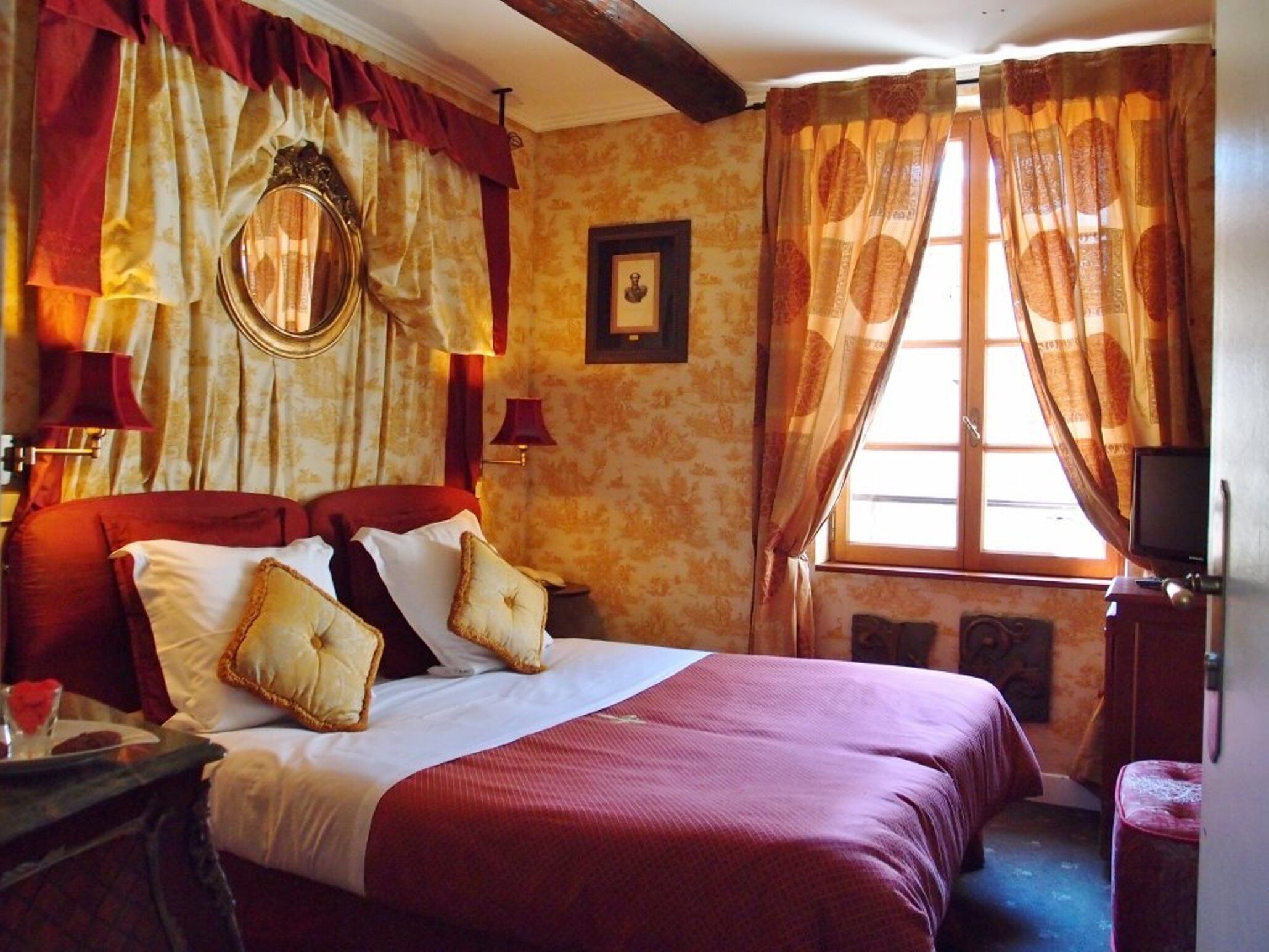 Une chambre d’hôtel avec un grand lit, des rideaux rouges, un miroir et une télévision.