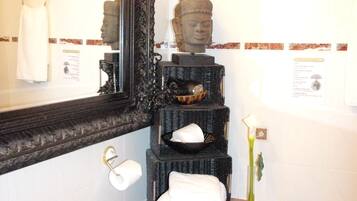 Un baño con un espejo grande y decorado, un lavamanos con artículos de tocador, una estatua de Buda y un cuadro en la pared.