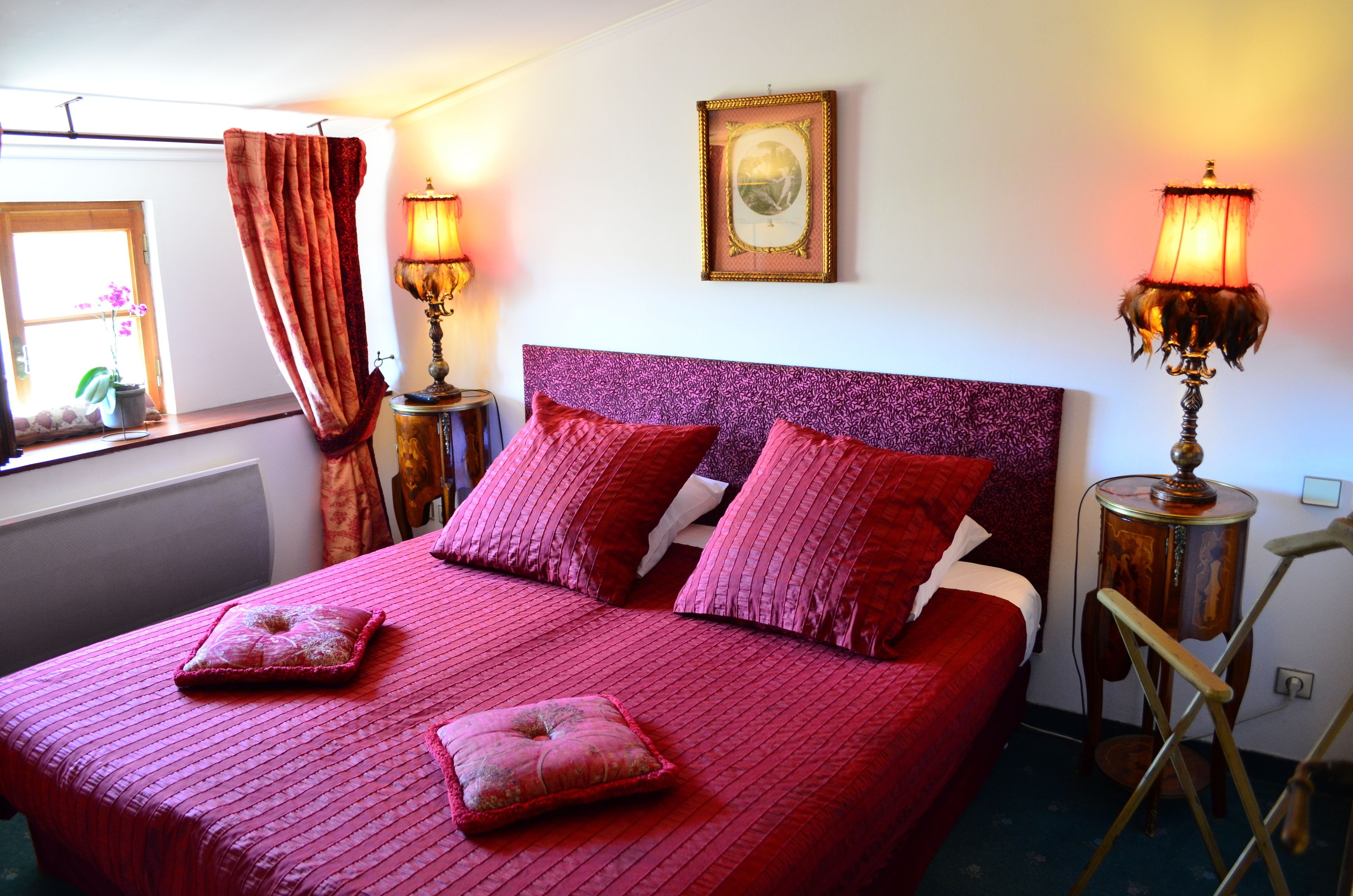 A bed with a purple headboard, two bedside lamps, and a window with curtains.
