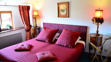 A bed with a purple headboard, two bedside lamps, and a window with curtains.