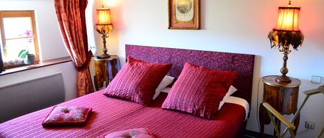 A bed with a purple headboard, two bedside lamps, and a window with curtains.