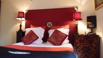 A bed with red and white bedding, two red lamps, a decorative wall hanging, and a wooden nightstand with a telephone.