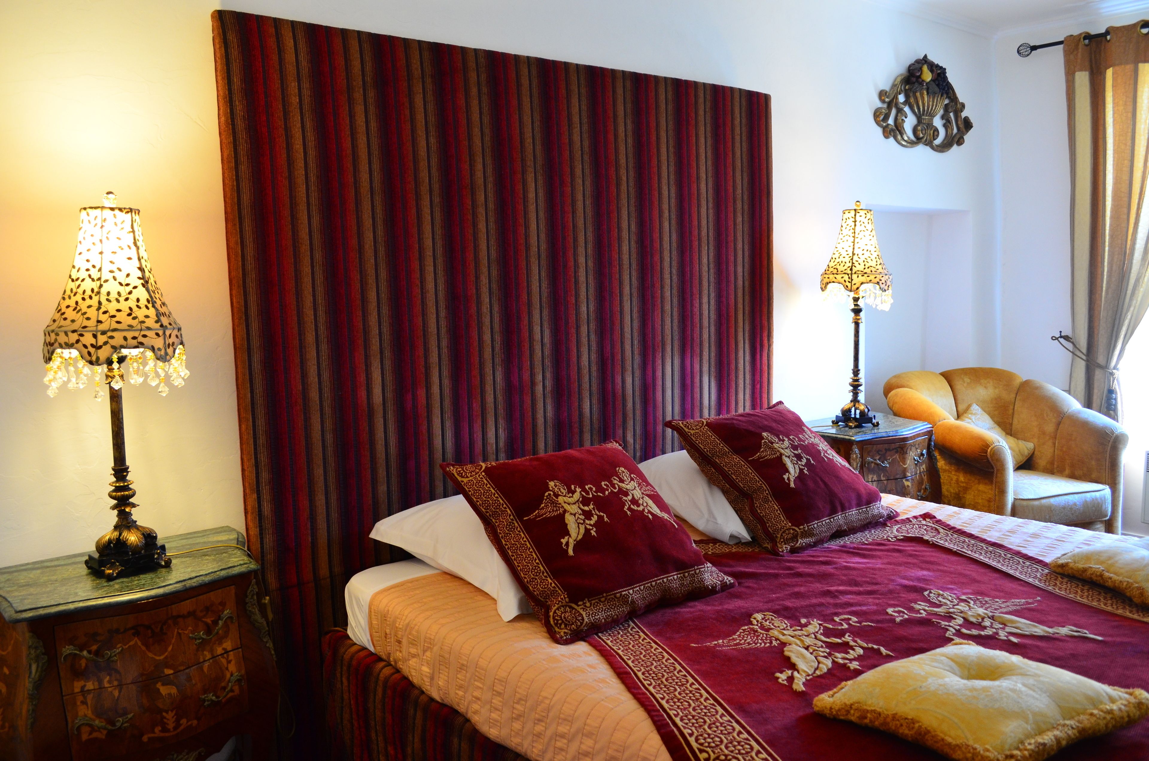 A hotel room with a large bed, two bedside lamps, a chair, and a curtain.