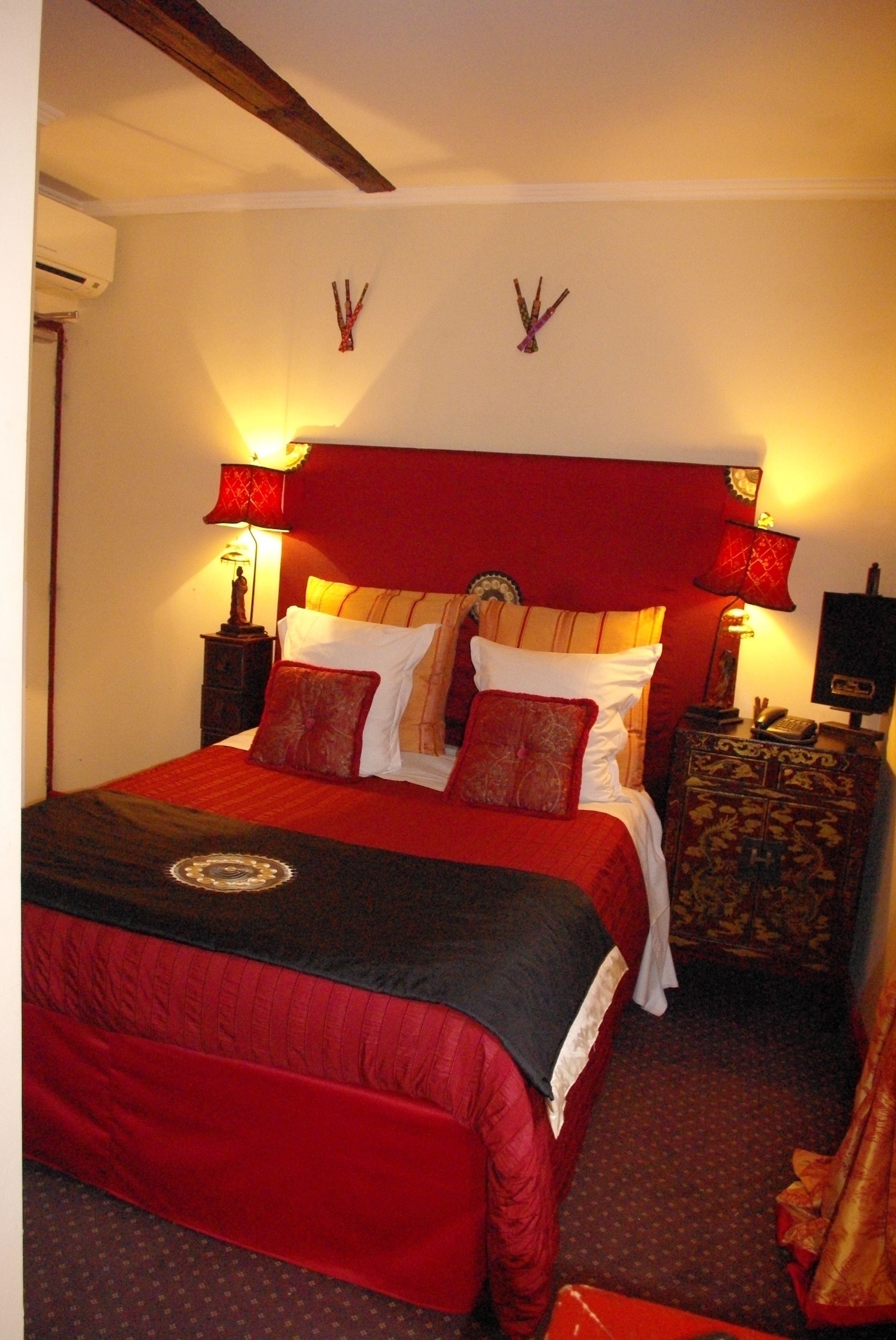 Una cama con ropa de cama roja, dos mesitas de noche con lámparas y un reloj fijado a la pared.