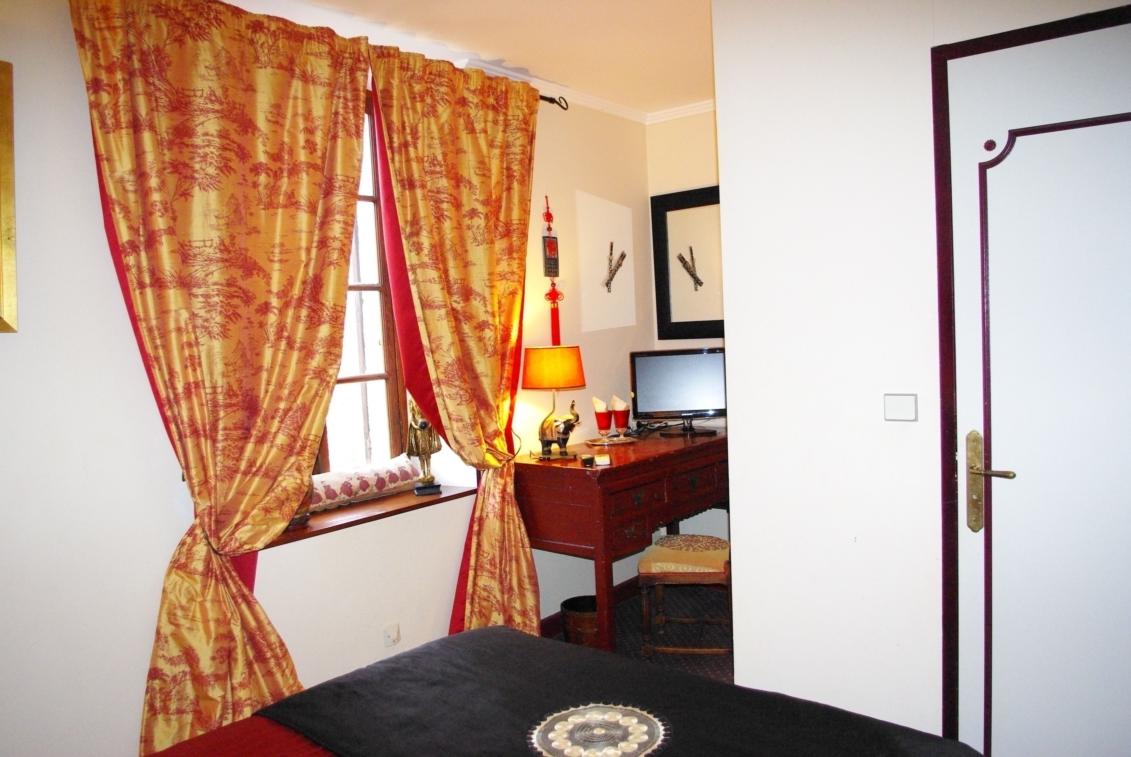 Un dormitorio con cama, un escritorio con computadora, una ventana con cortinas y una puerta.