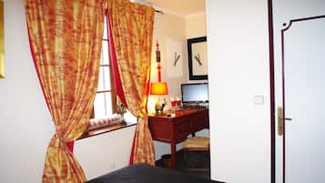 Un dormitorio con cama, un escritorio con computadora, una ventana con cortinas y una puerta.
