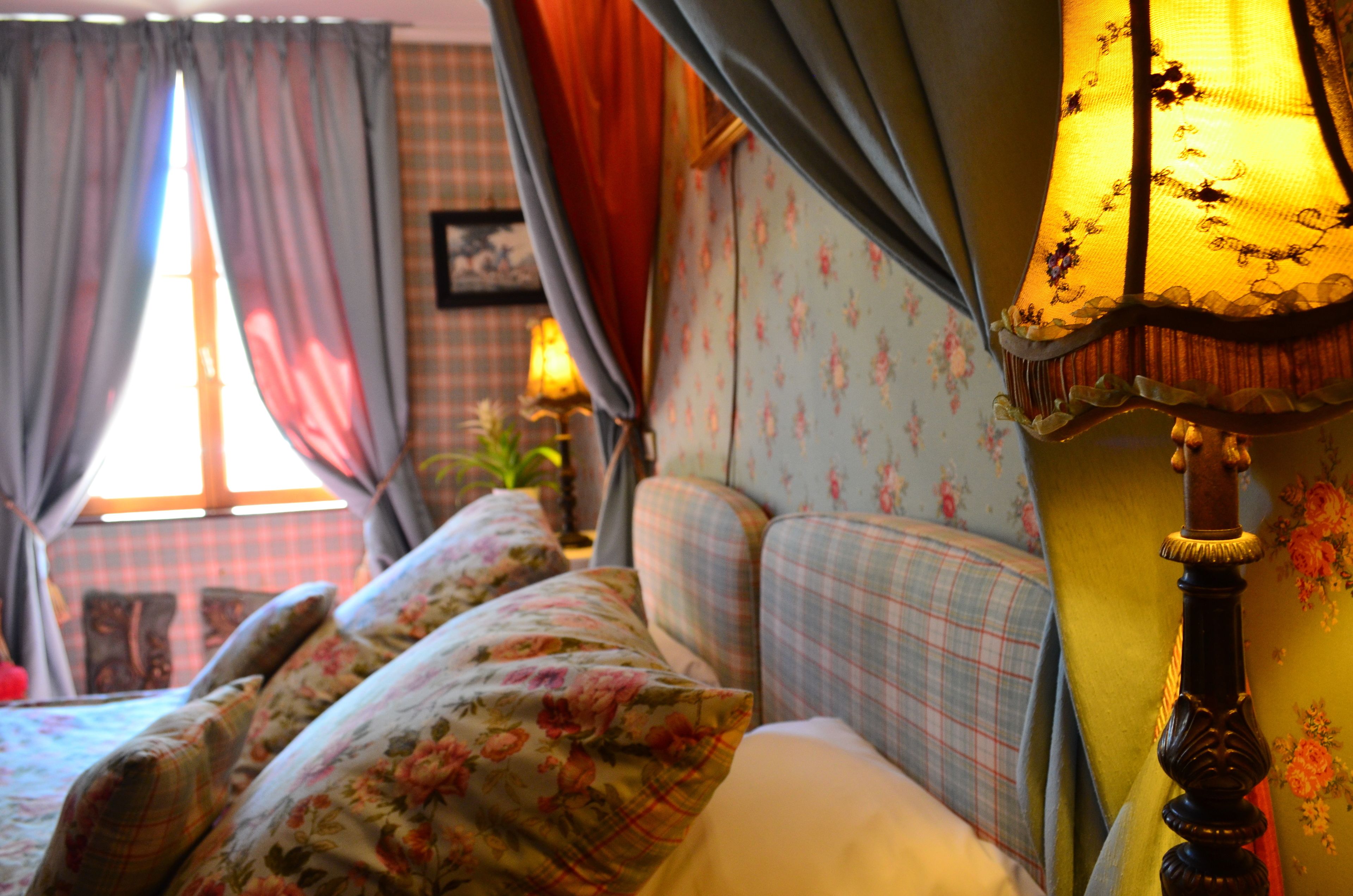 A bedroom with floral bedding, a window with curtains, and a bedside lamp.