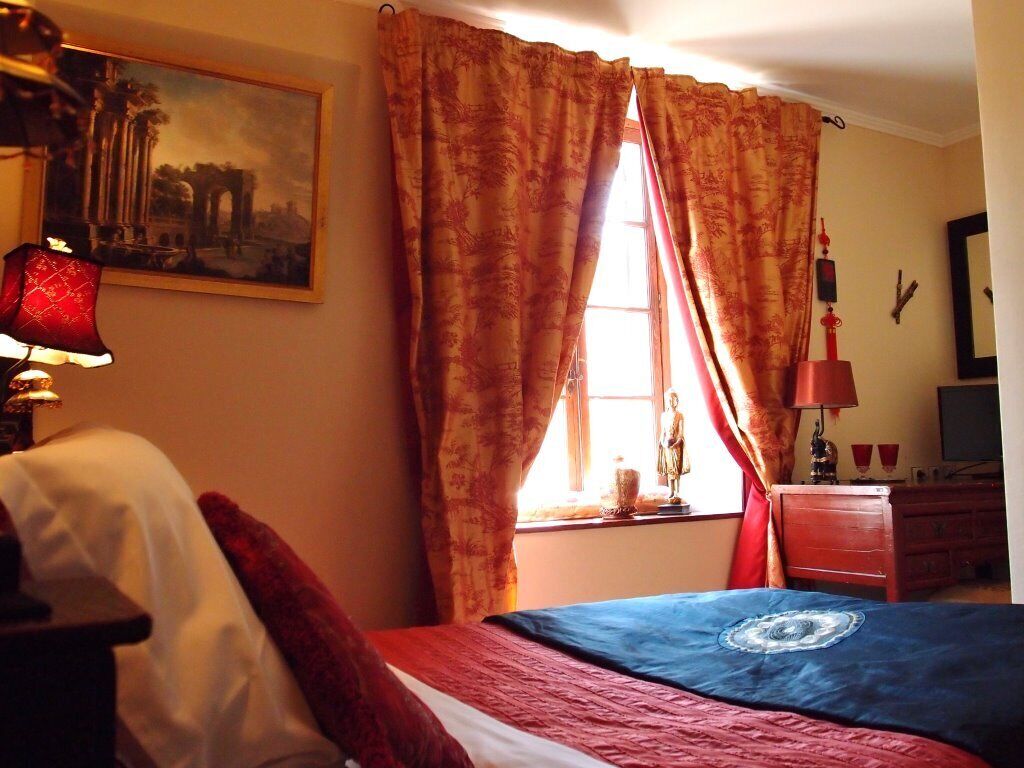 A bedroom with a bed, a window with curtains, a lamp, a dresser, and a painting on the wall.
