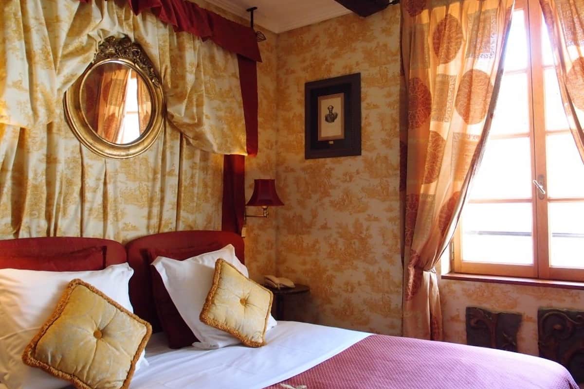 Une chambre d’hôtel avec un grand lit, des rideaux rouges, un miroir rond et un tableau encadré au mur.
