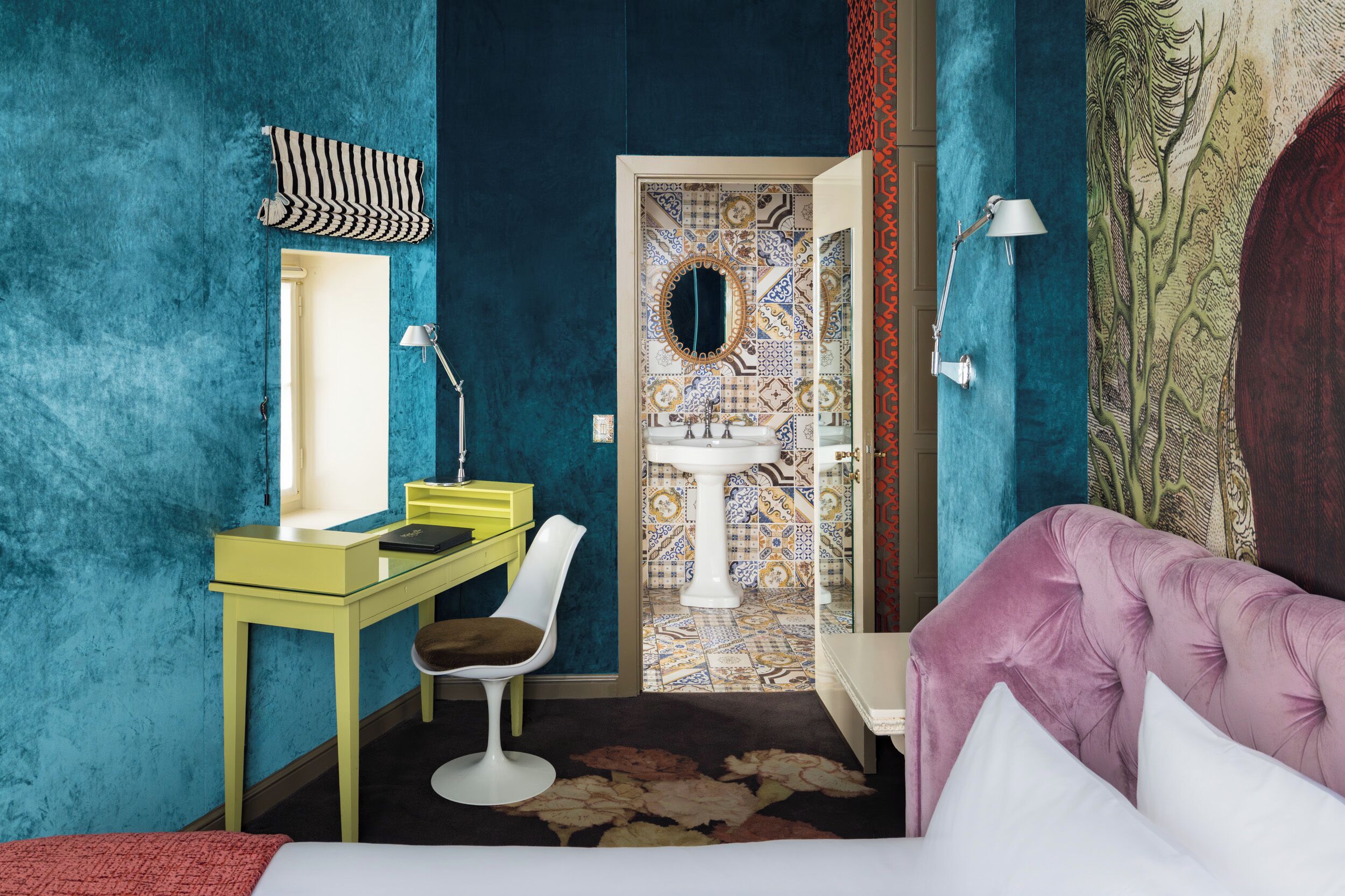 Una habitación con pared color aguamarina, escritorio amarillo, silla blanca, sofá púrpura y alfombra estampada.