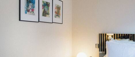 A hotel room with a bed, a nightstand with a lamp, and three framed artworks on the wall.