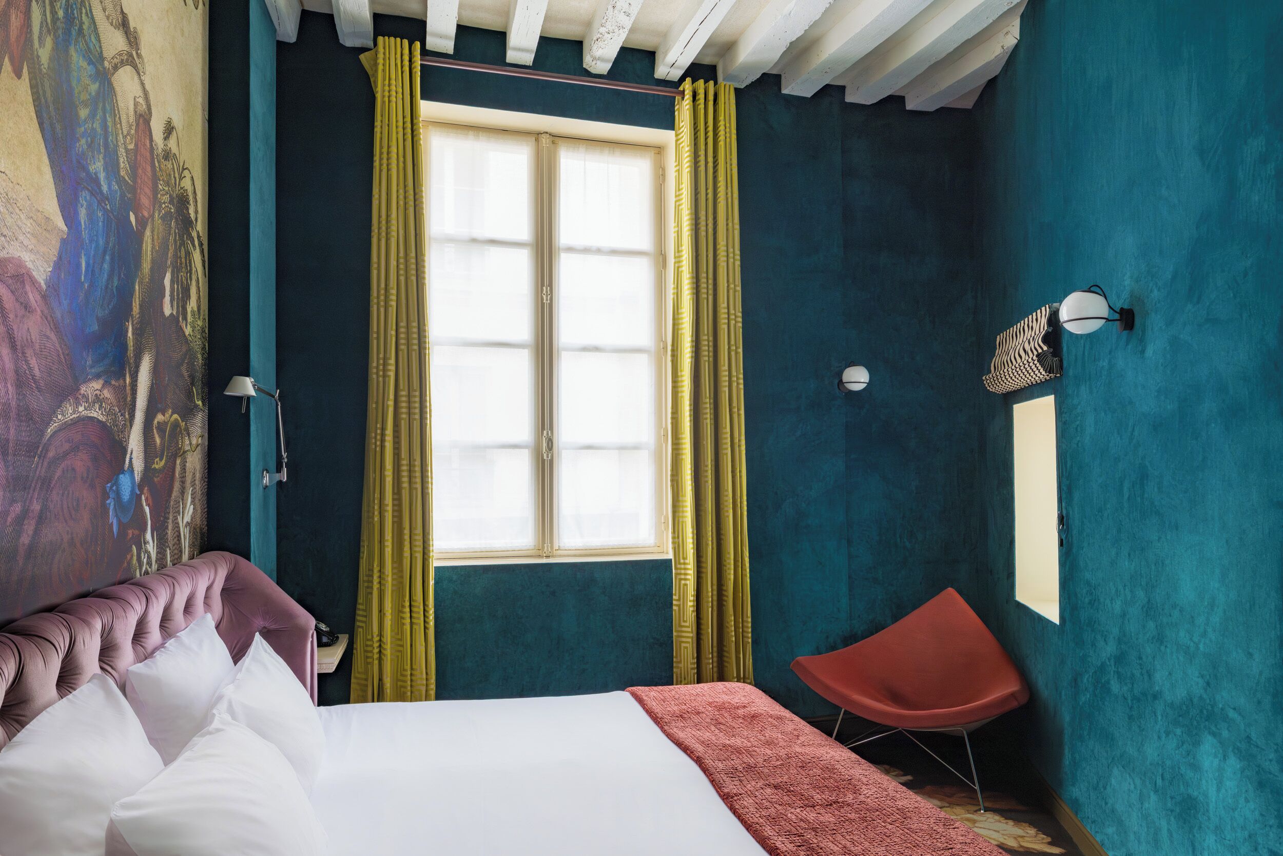 Een slaapkamer met een bed, een rode stoel, een raam met gele gordijnen en een muur met een reliëf muurschildering.
