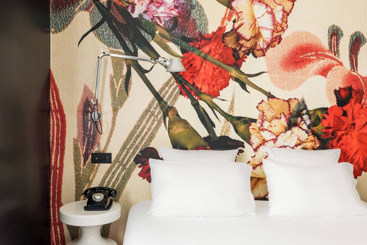 A bed with white pillows and a nightstand with a lamp and an old-fashioned telephone.