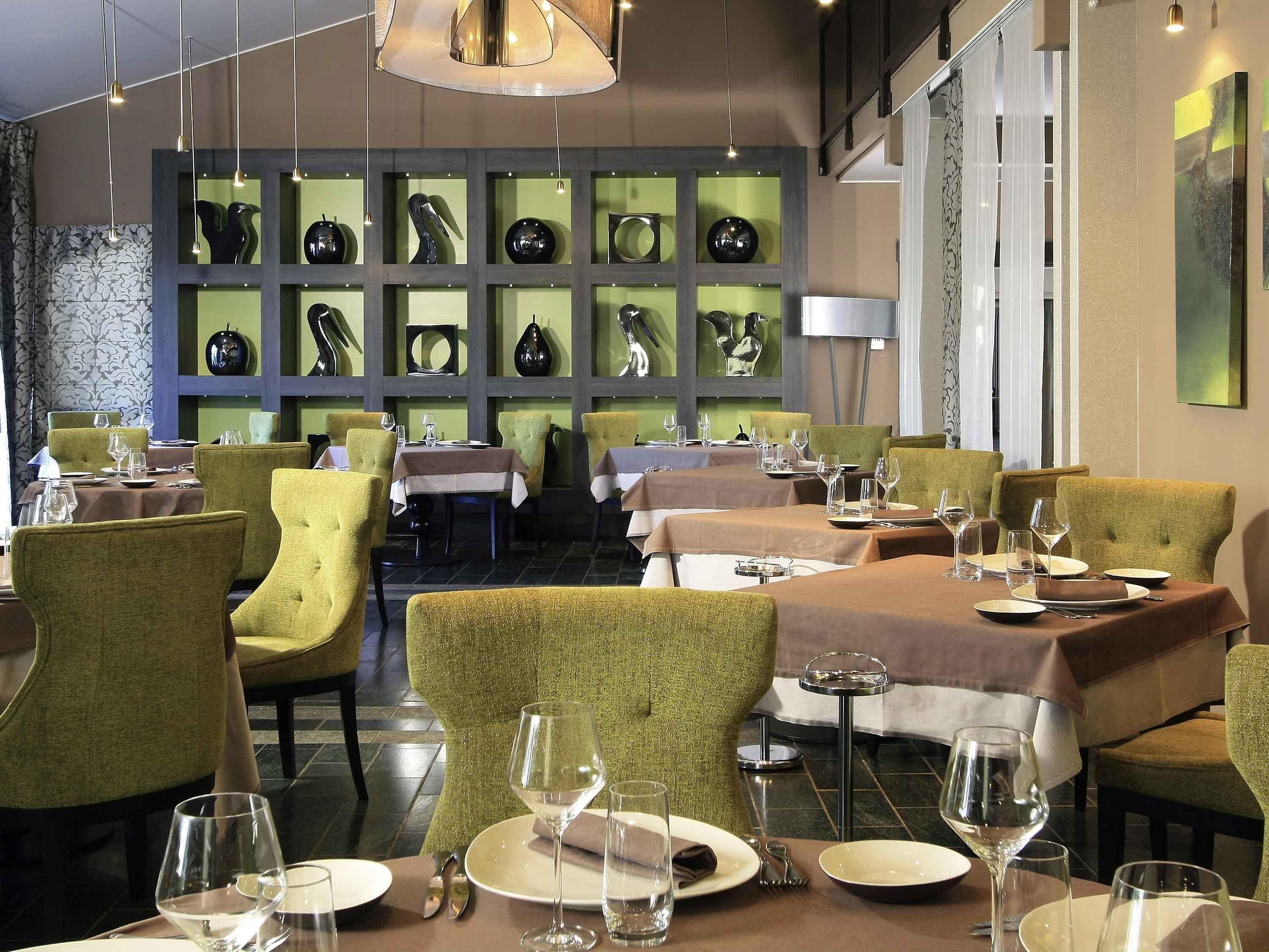 A restaurant with green upholstered chairs, tables set with plates and glasses, and a wall of decorative vases.