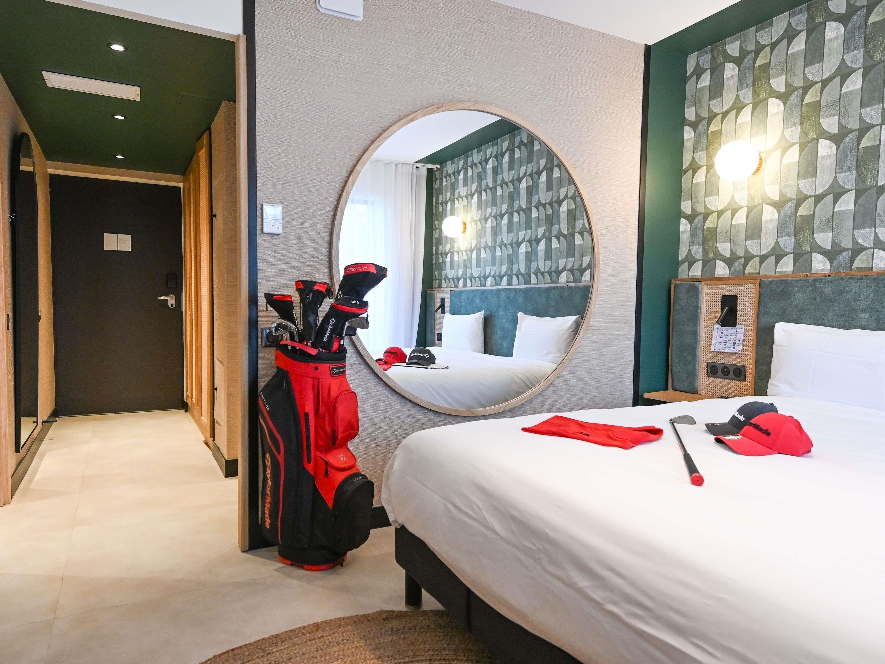 Una habitación de hotel con una cama, un espejo, un bolso de golf y una pared con un diseño geométrico.