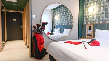 A hotel room with a bed, a mirror, a golf bag, and a wall with a geometric pattern.