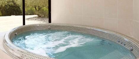 Un jacuzzi con suelo de mosaico, rodeado por una pared de baldosas color crema.