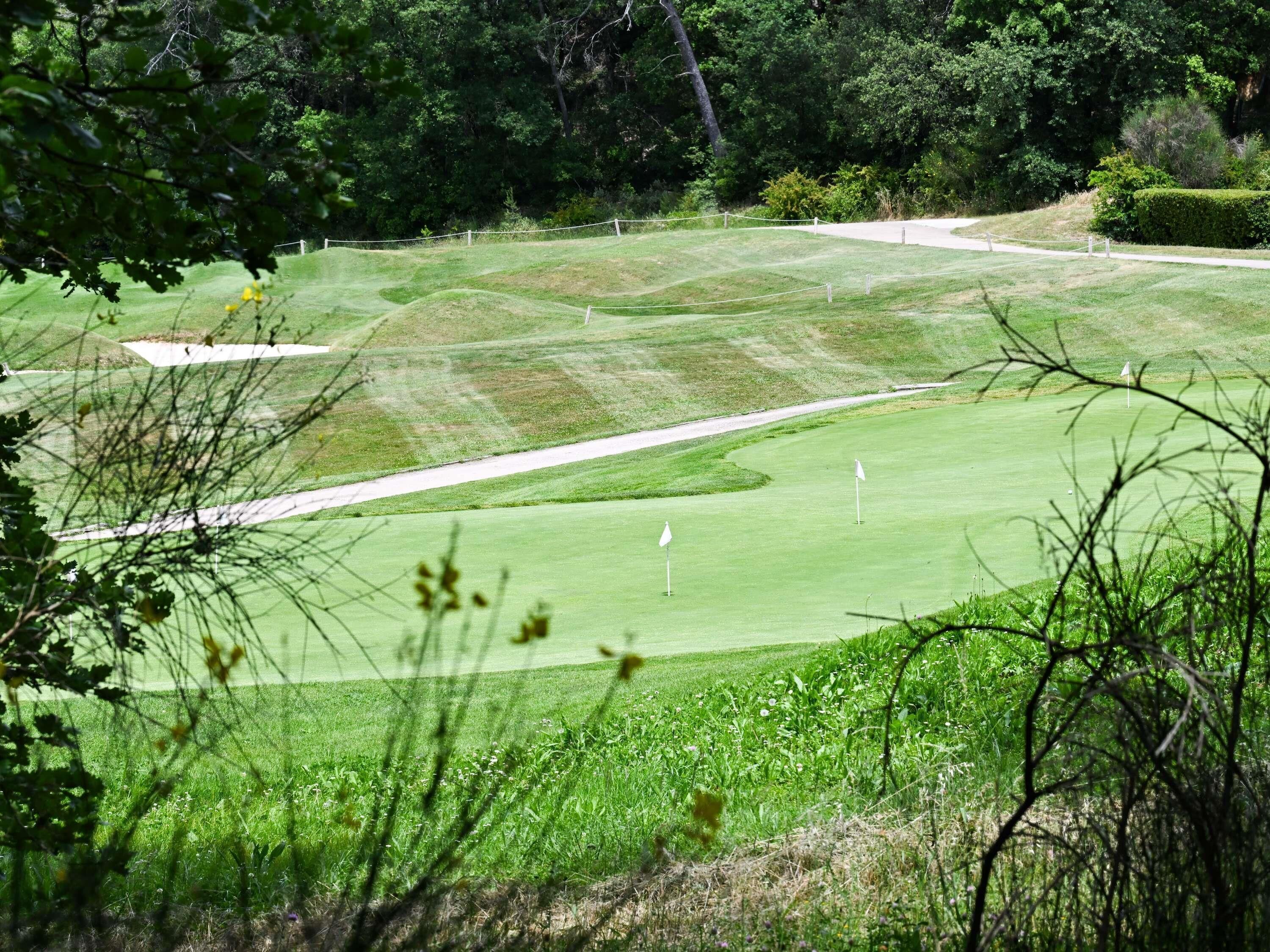 Un parcours de golf comportant plusieurs trous, un terrain bien entretenu et une zone boisée en arrière-plan.