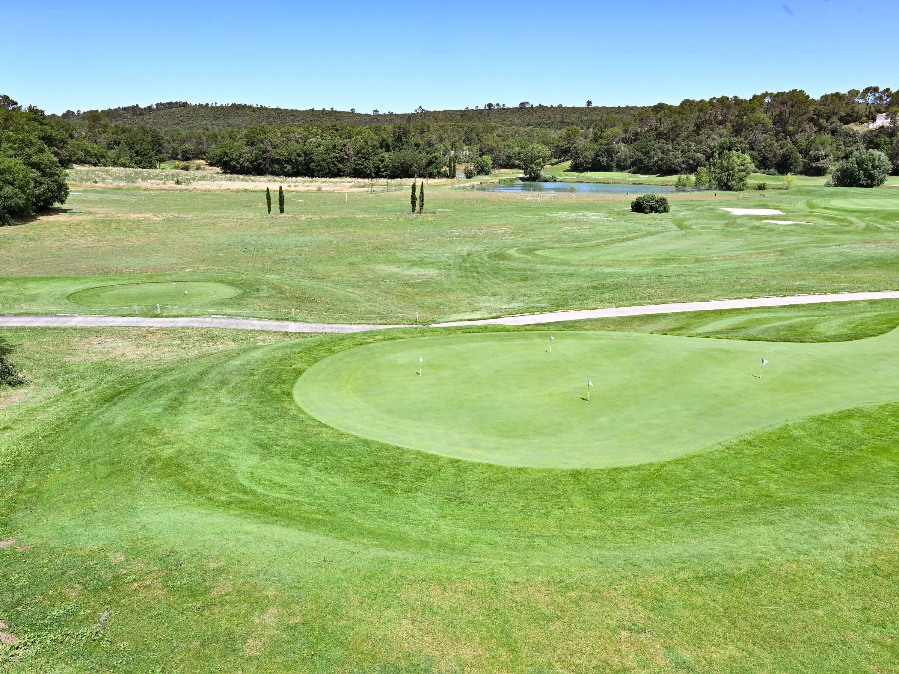 A golf course with well-maintained fairways, sand bunkers, and a pond in the background.