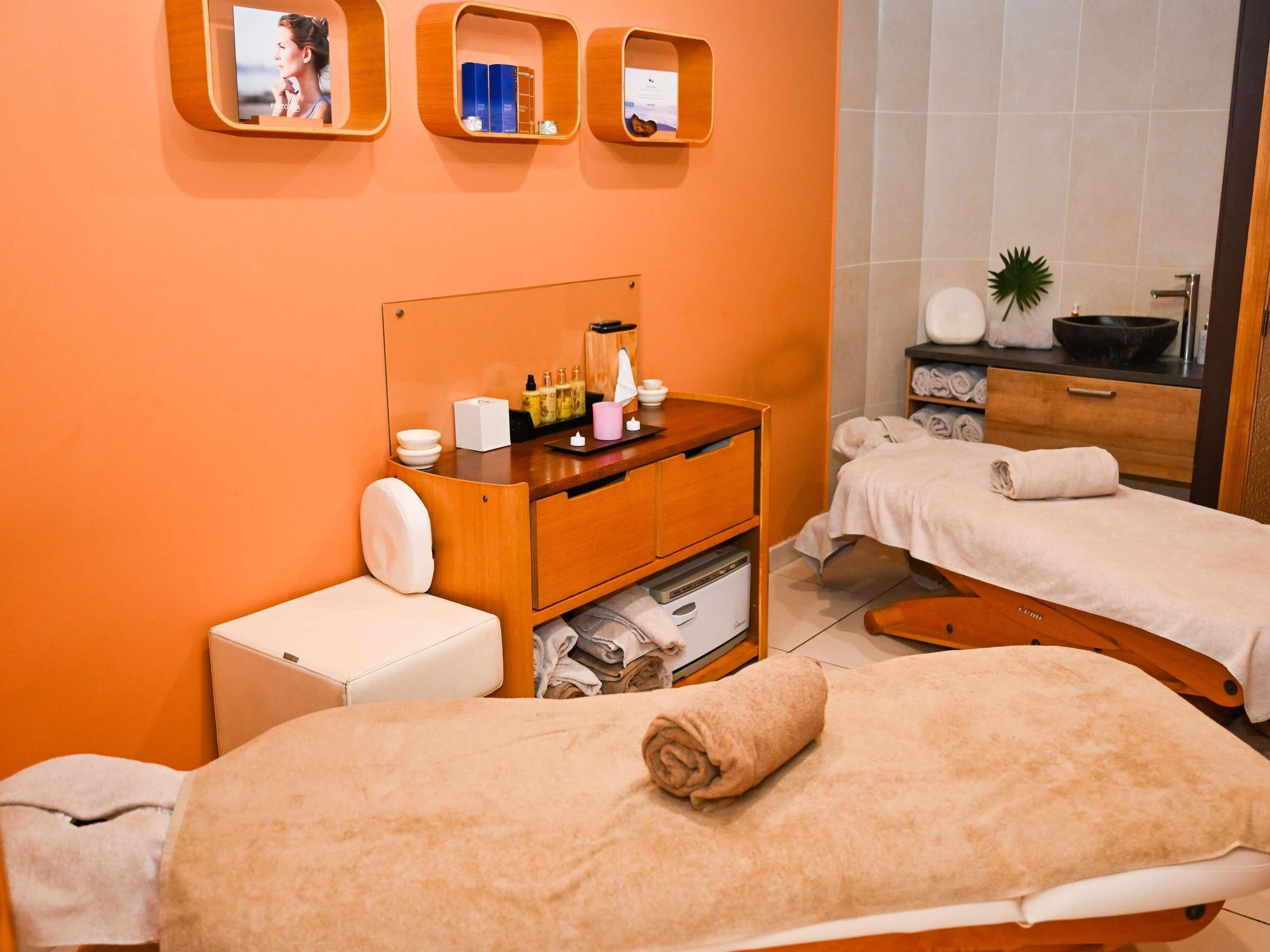 A hotel room with two beds, a wooden dresser with toiletries, a small white cabinet, and a mirror with photos.
