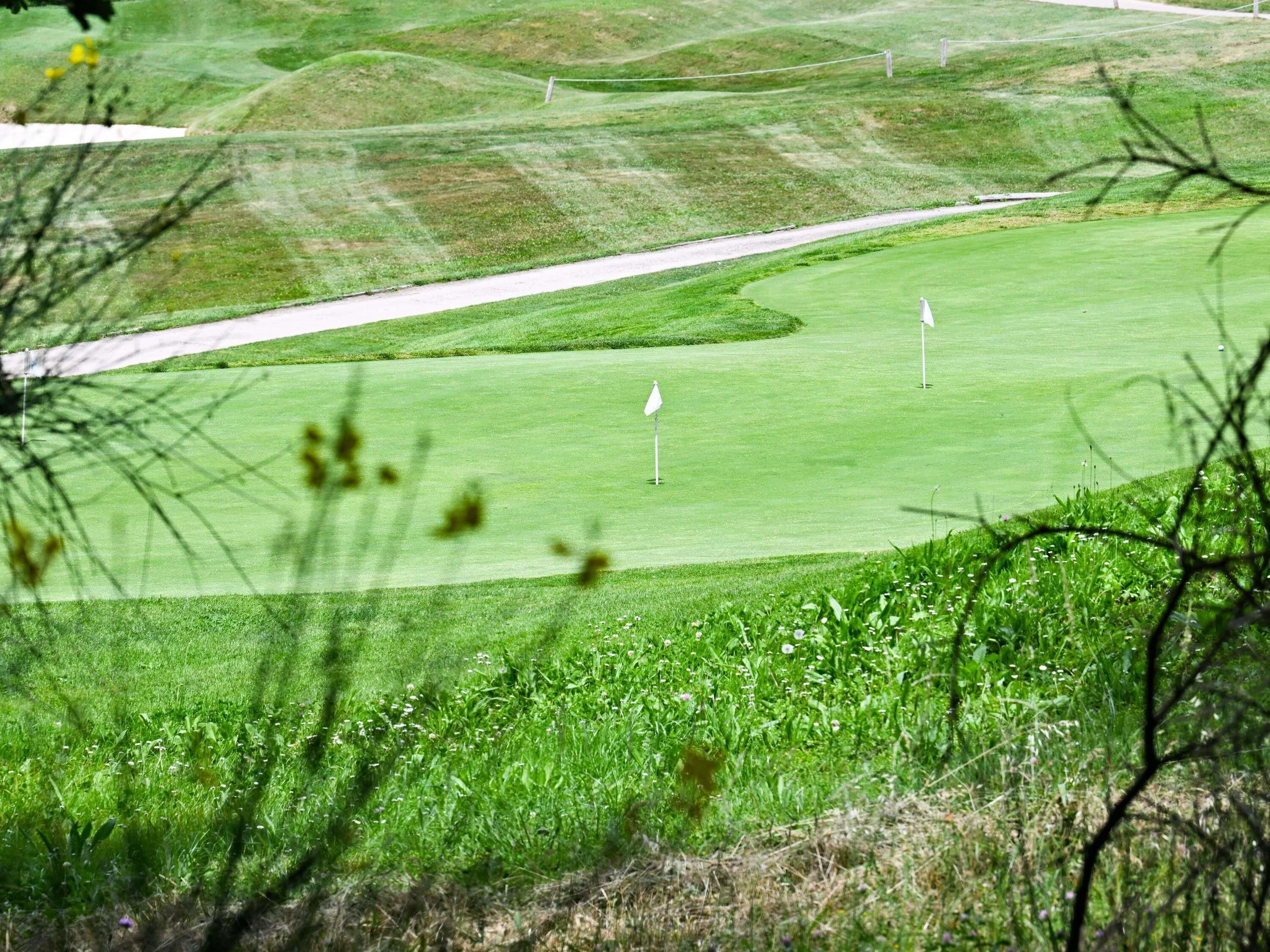 Um campo de golfe com greens bem cuidados, um bunker de areia e duas bandeiras marcando os buracos.