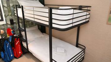 A bunk bed with white bedding and a black metal frame. There are two bags on the floor beside the bed.