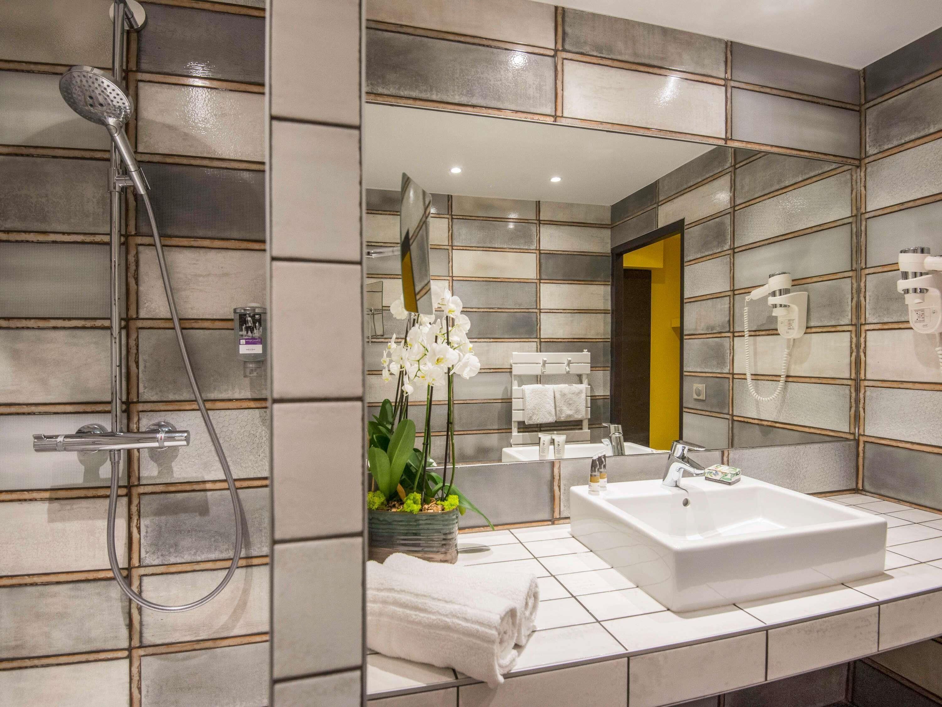 A modern bathroom with a large mirror, a shower, a sink, and a toilet.