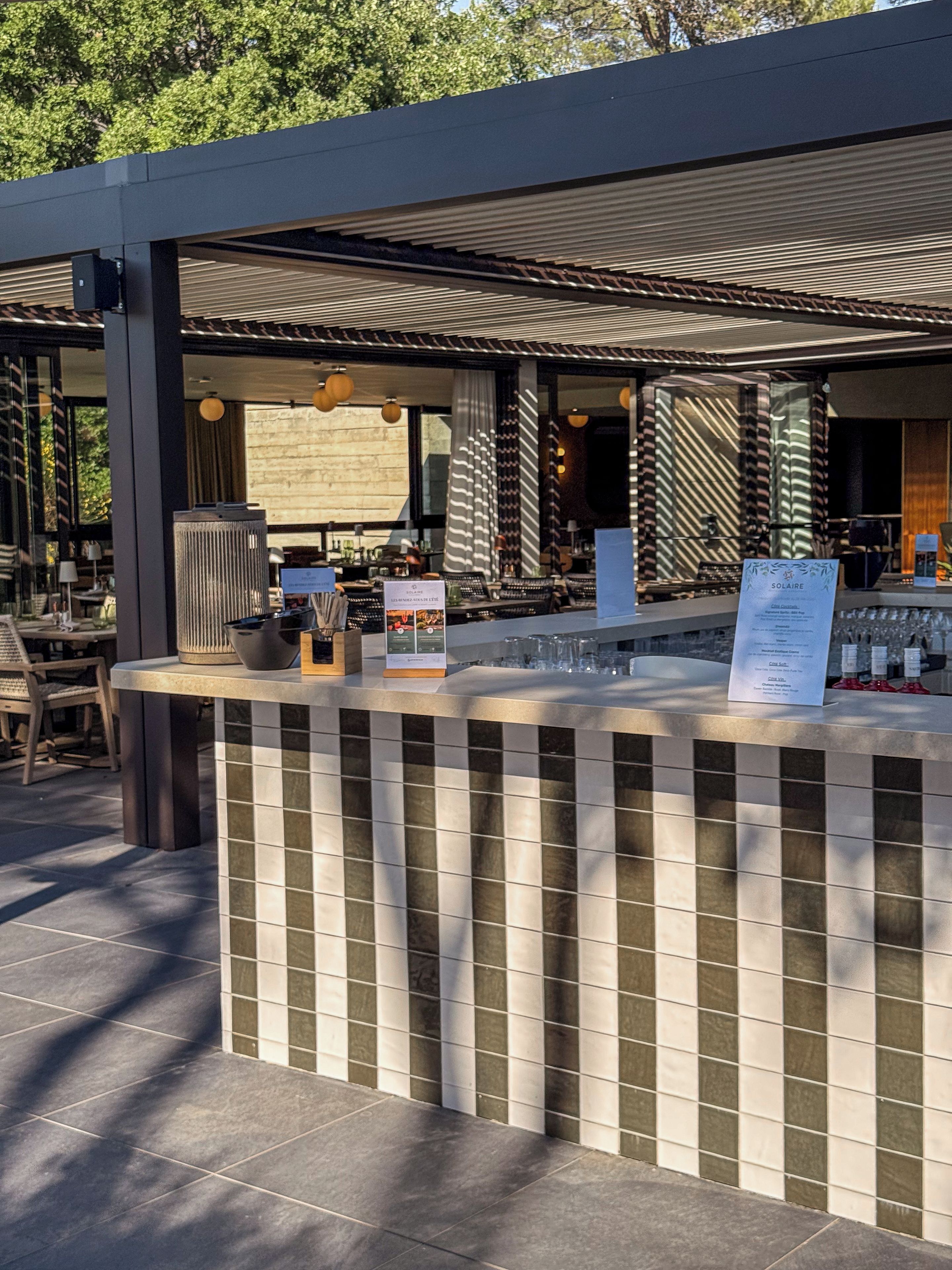 Un espace bar extérieur doté d’un comptoir carrelé, de sièges et d’une structure en forme de pergola.