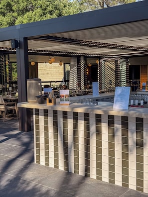 Un área de bar al aire libre con mostrador de azulejos, asientos y una estructura de pérgola.