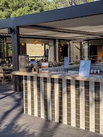 Un área de bar al aire libre con mostrador de azulejos, asientos y una estructura de pérgola.