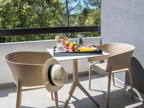 A balcony with two chairs, a table with breakfast items, and a view of trees.