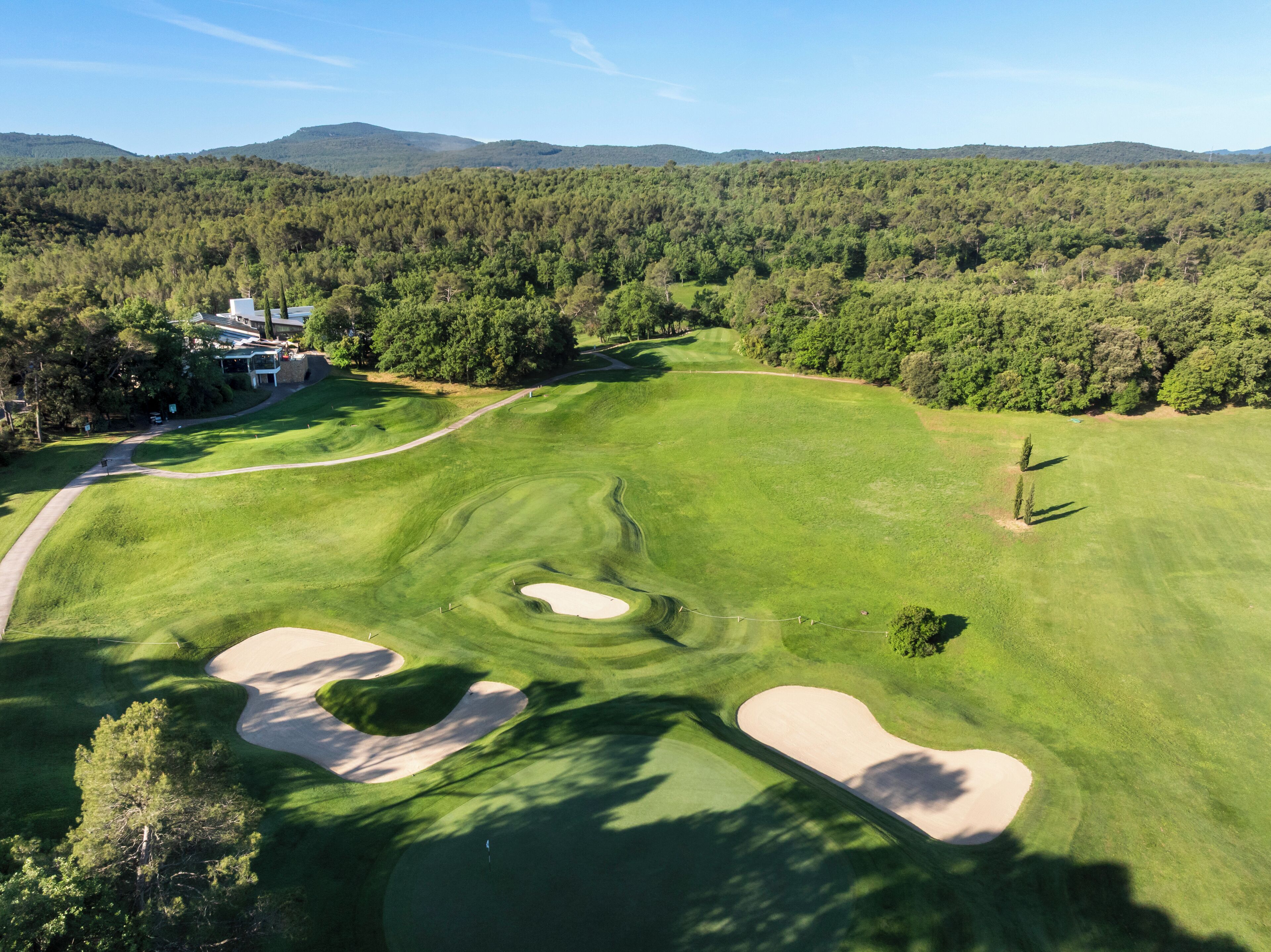 A golf course with sand bunkers, a clubhouse, and a forested backdrop.