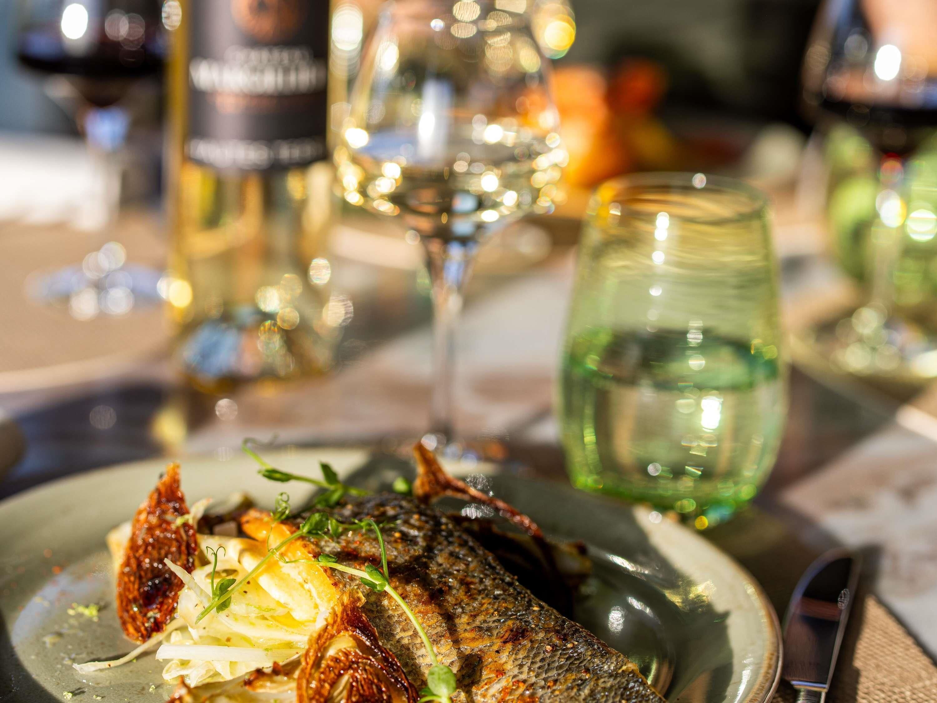 Un piatto di cibo con del pesce, guarnizioni e un bicchiere di vino bianco.