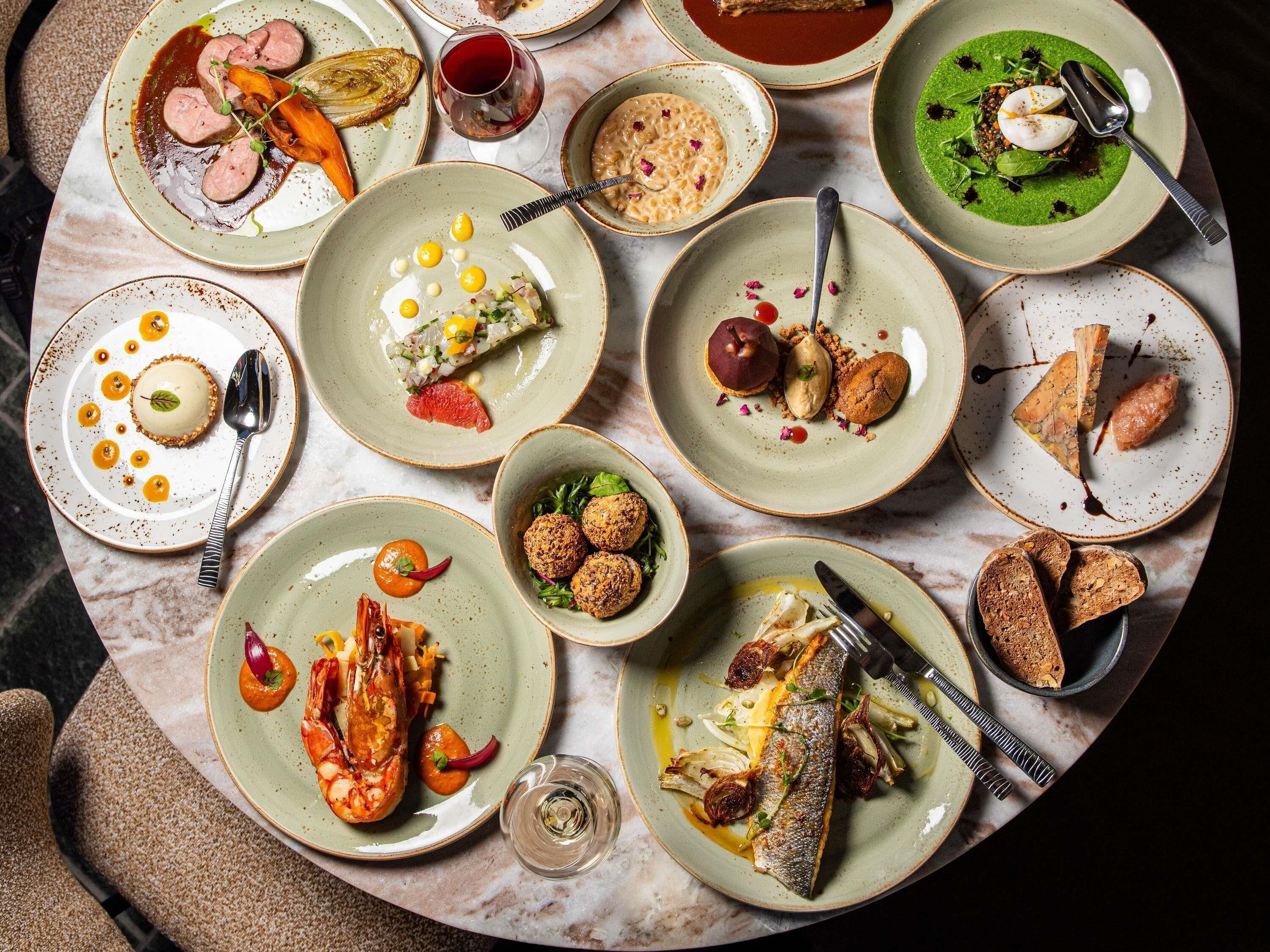 Diversos platos con mariscos, verduras y postres, dispuestos sobre una mesa de mármol.