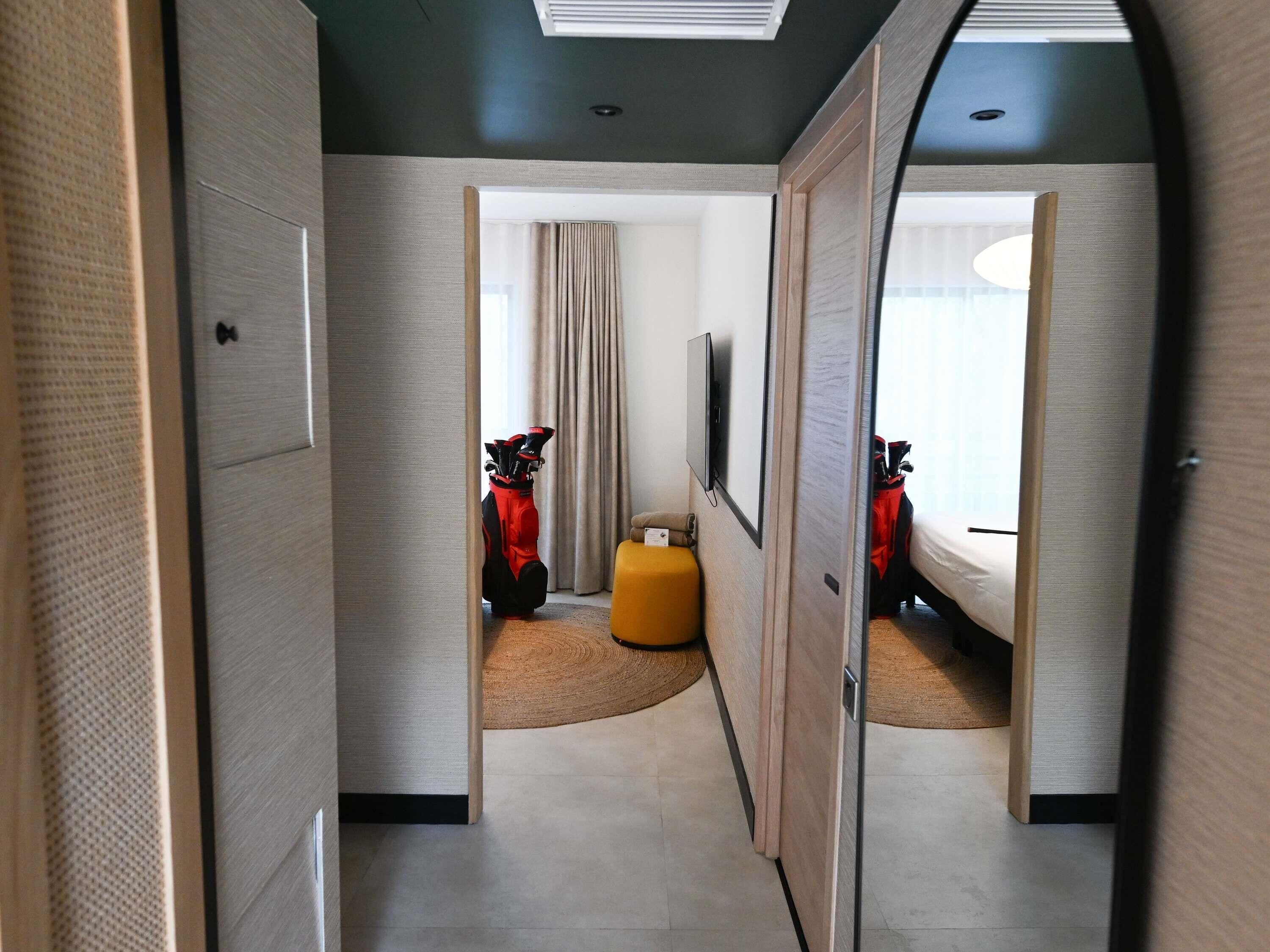 Una habitación de hotel moderna con una cama grande, televisión, bolsa de golf y un pequeño espacio para sentarse.