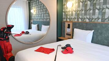 Une chambre d’hôtel avec un miroir rond, un lit avec du linge de lit blanc, un sac de golf et une casquette rouge posée sur le lit.